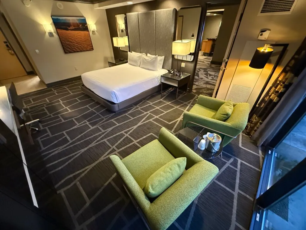 Two green single seat chairs near the window pointed at the King bed, which is in the background.