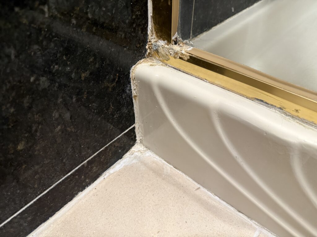 A corner of the shower where the caulking looks battered and worn.