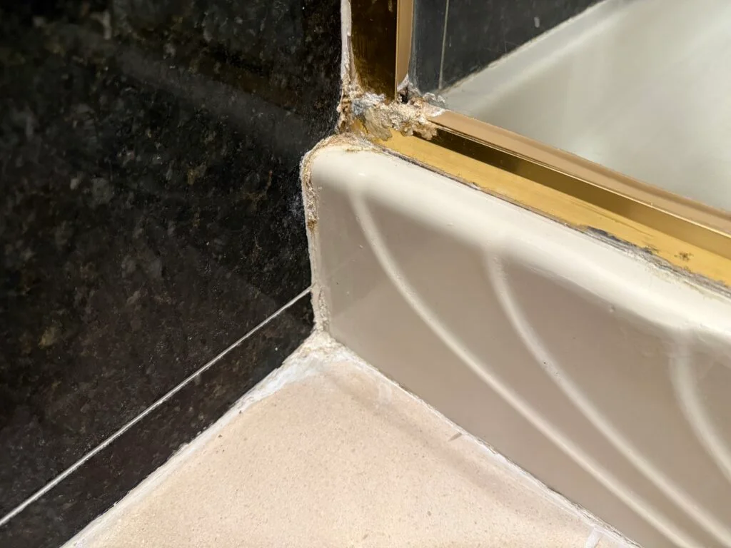 A corner of the shower where the caulking looks battered and worn.