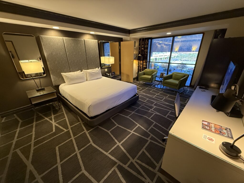 A wide angle shot of the room with the king bed in the middle and window in the background.