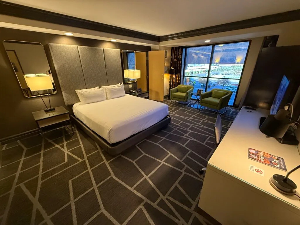 A wide angle shot of the room with the king bed in the middle and window in the background.