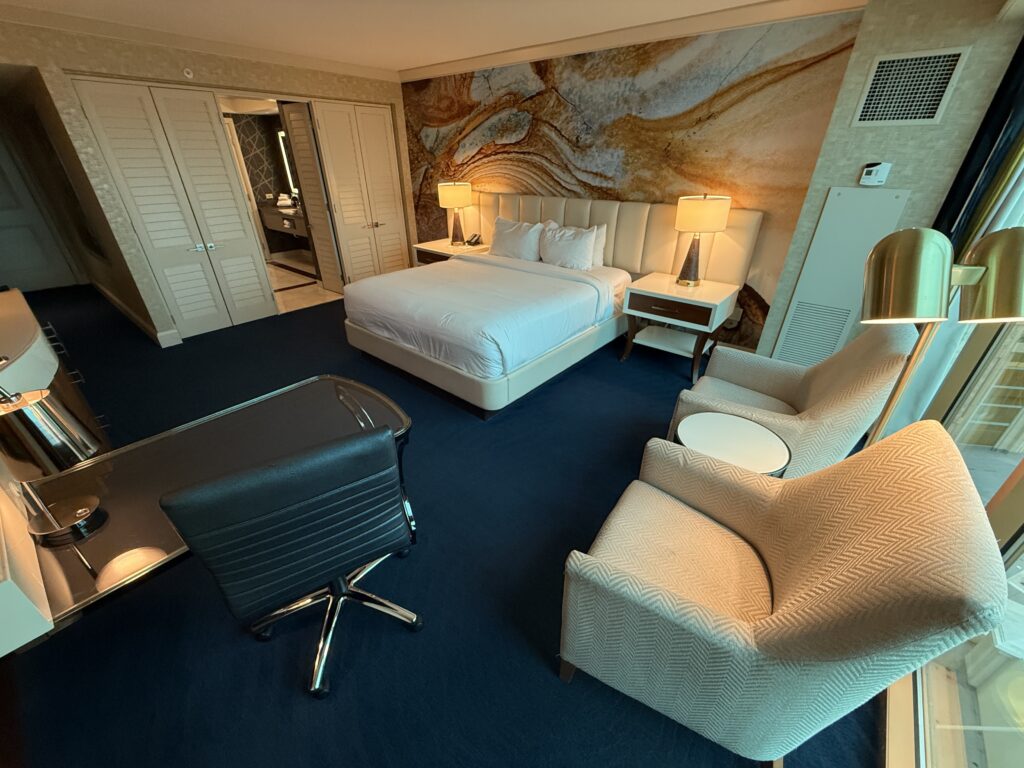 A king bed and bathroom entrance with 2 chairs in the foreground.