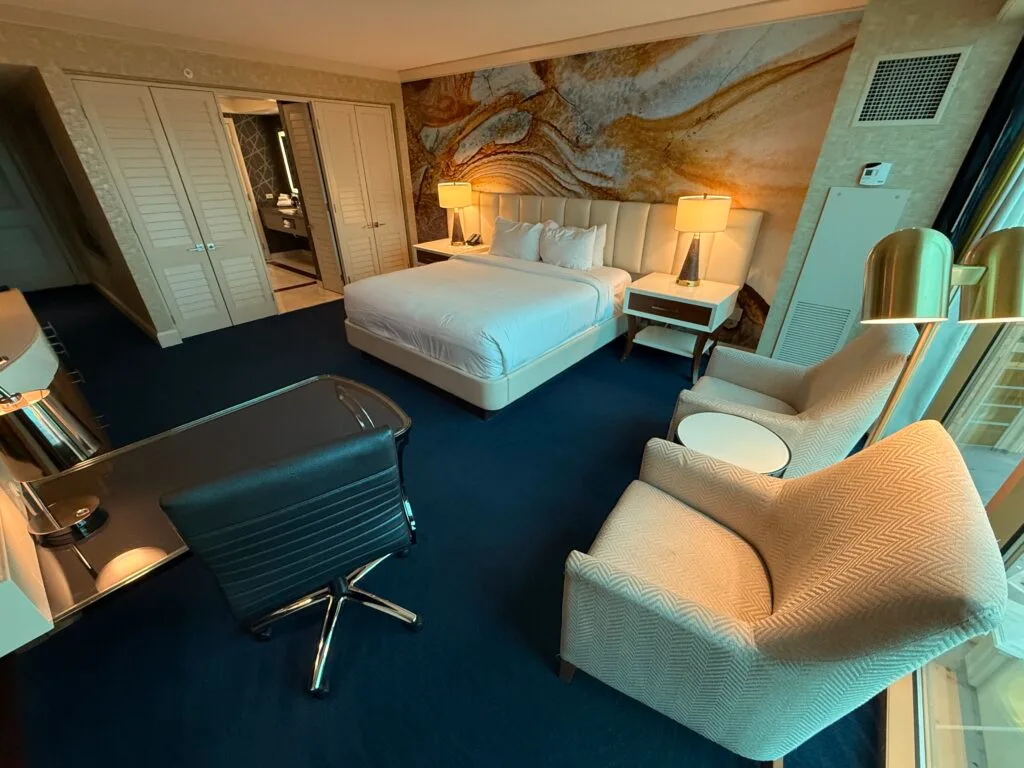 A king bed and bathroom entrance with 2 chairs in the foreground.