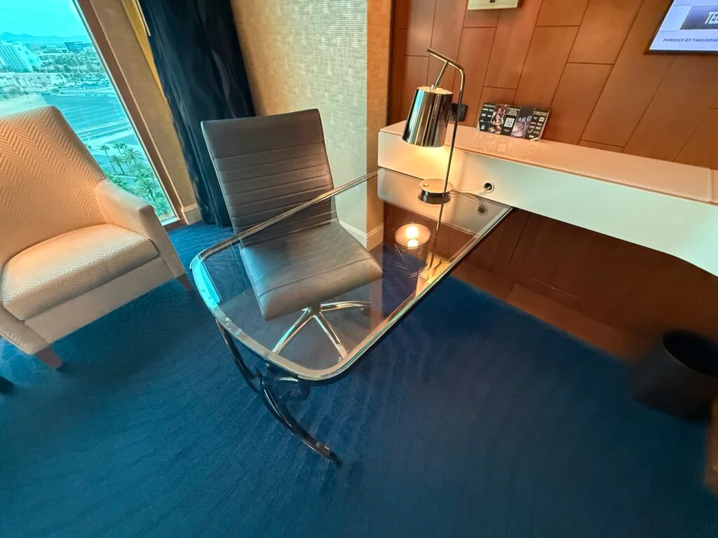 A glass workdesk aith a rolling chair tucked underneath.