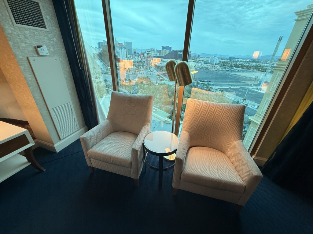 2 single seat chairs with a small table between them positioned in front of the windows.