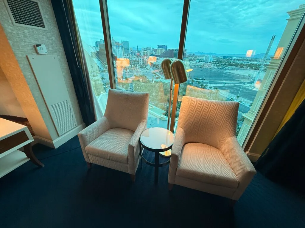 2 single seat chairs with a small table between them positioned in front of the windows.