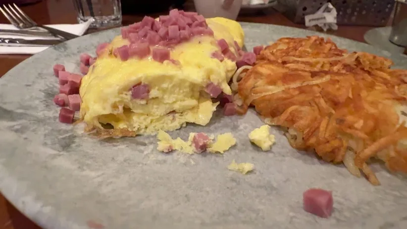 An omelet, topped with a pile of cubed ham alongside hashbrowns. 