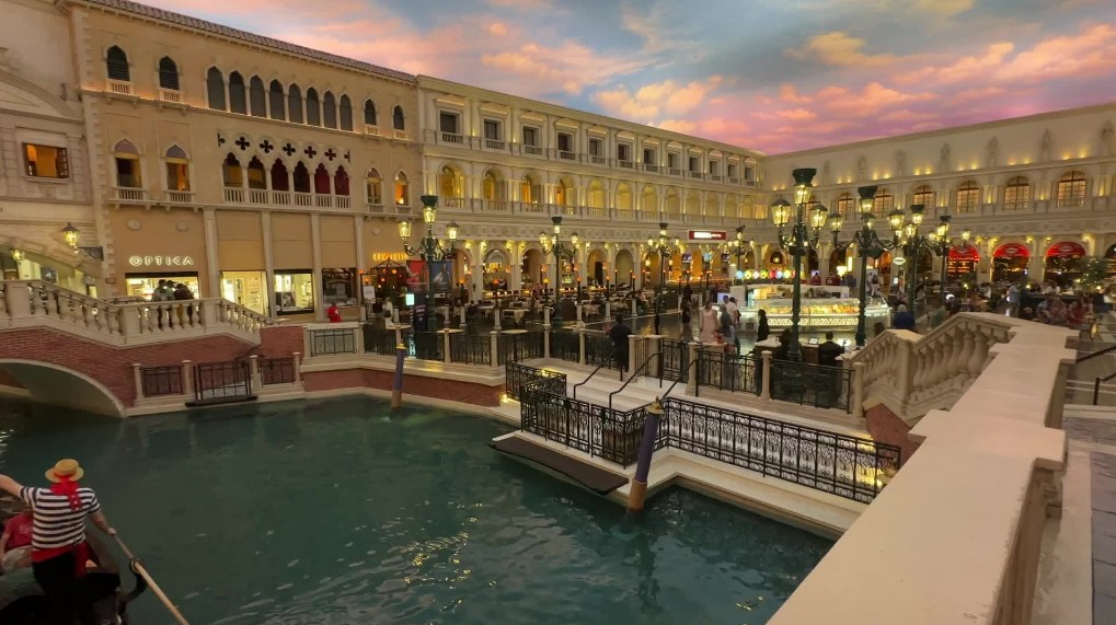 A canal in the foreground, and a replica st. mark's square in the background with a painted blue sky.
