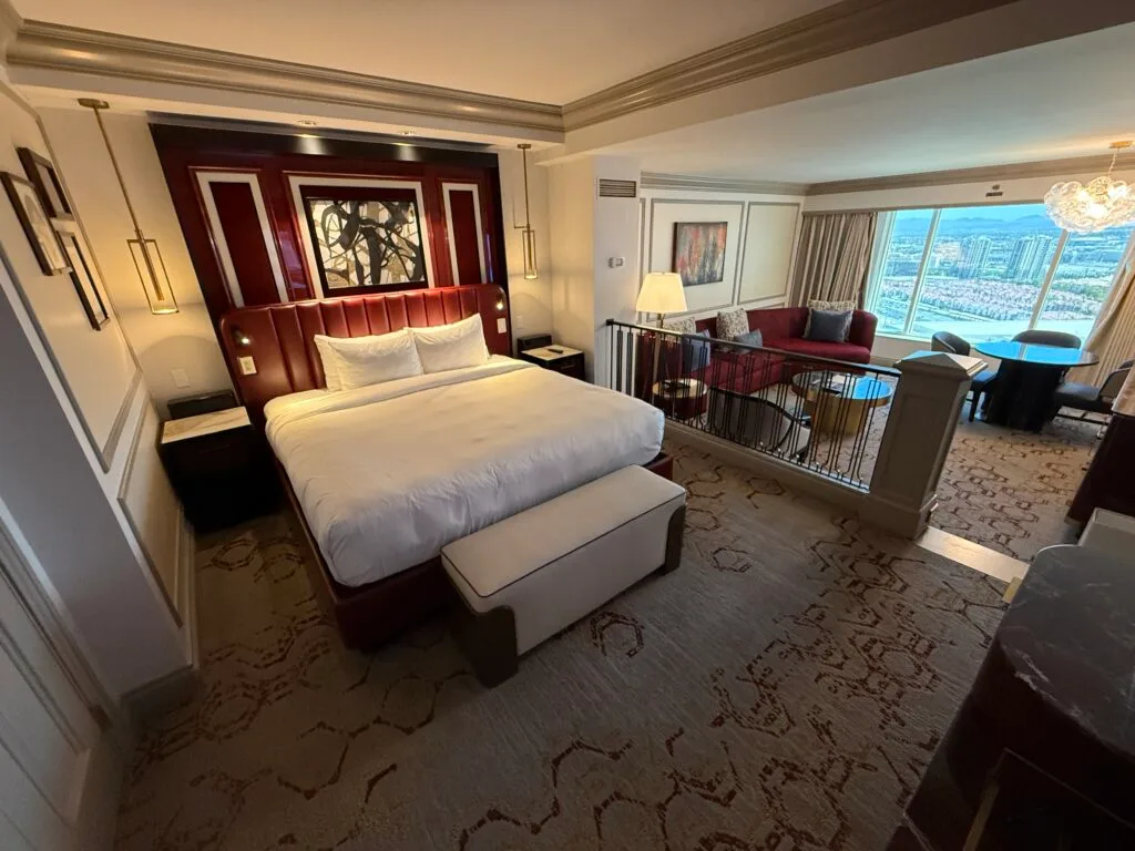 A king bed with a bench at the end. The bed is up against a red accent wall. 