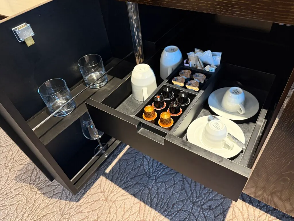 A pull out drawer stocked with coffee pods, cups and plates.