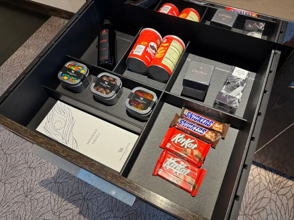 A pull out drawer stocked iwth dry minibar items like candy, nuts, and a small bottle of wine. 