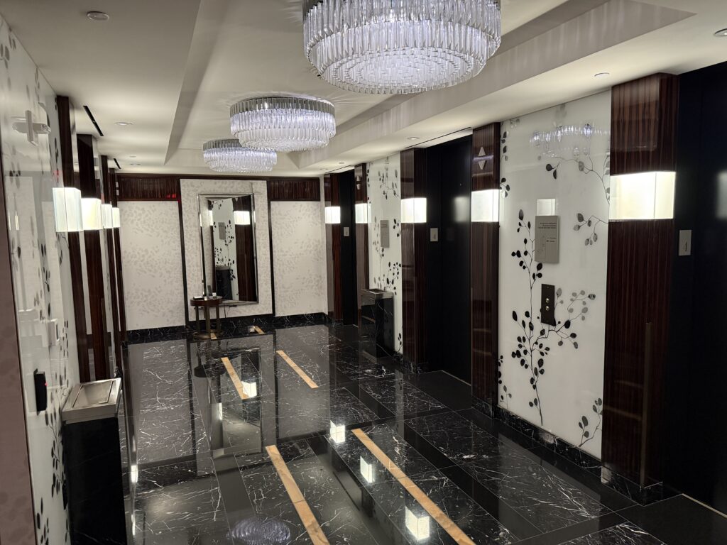 The elevbator lobby with glass chandeliers above, and dark stone flooring.