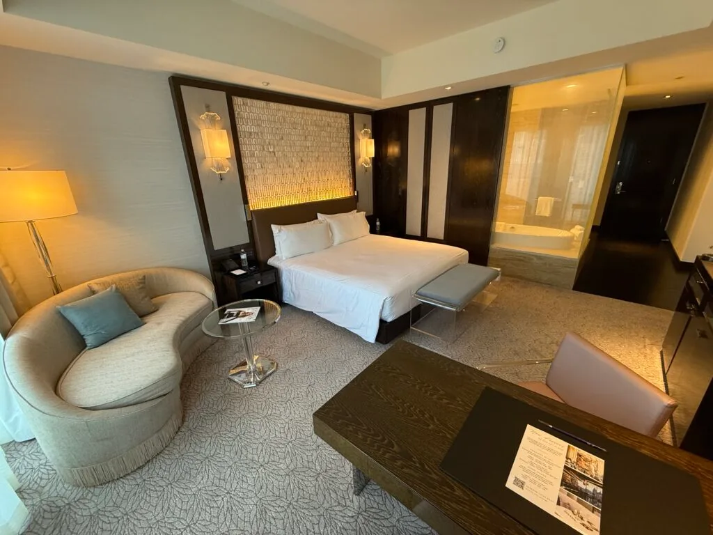 Another angle of the room that shows the king bed with a small kidney shaped couch to the left and a window into the bathroom to the right. 