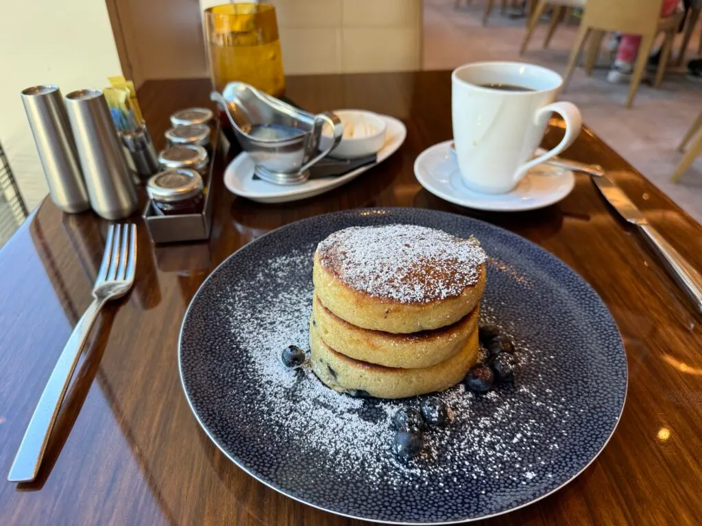A stack of 3 tiny pancakes on a blue plate that has a few blueberries on it. The pancakes are dusted with powdered sugar. 