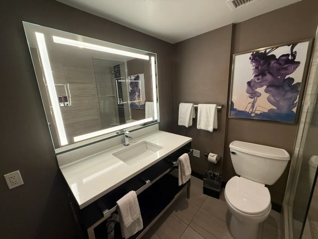 A single sink vanity with an illuminated mirror and toilet to the right. 