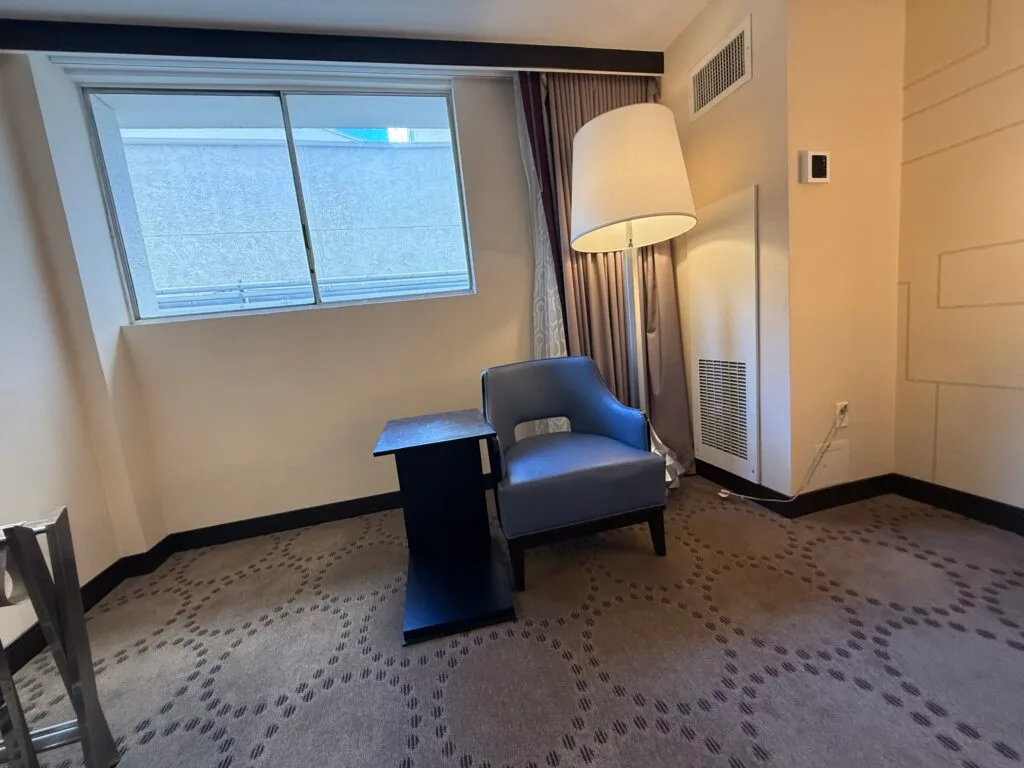 A single chair next a table underneath a lamp and the small window. 