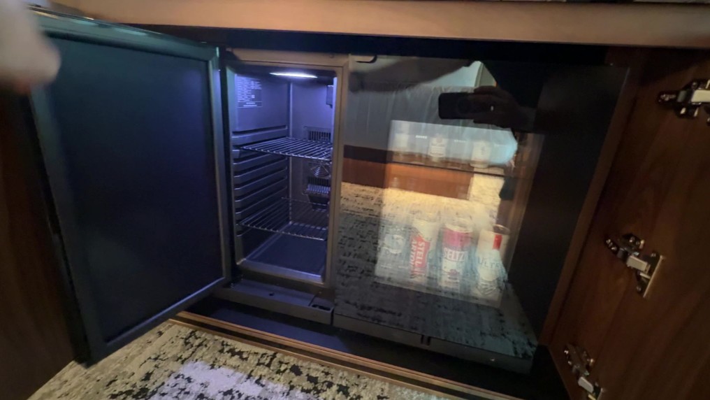 An empty mini fridge open next to a stocked mini bar fridge.