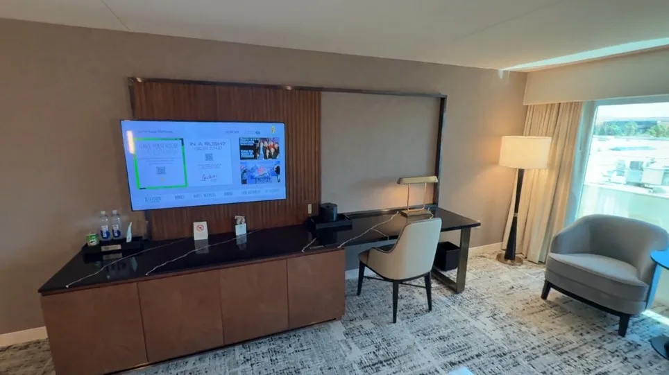 TV mounted on a stand next to a workdesk and chair. 