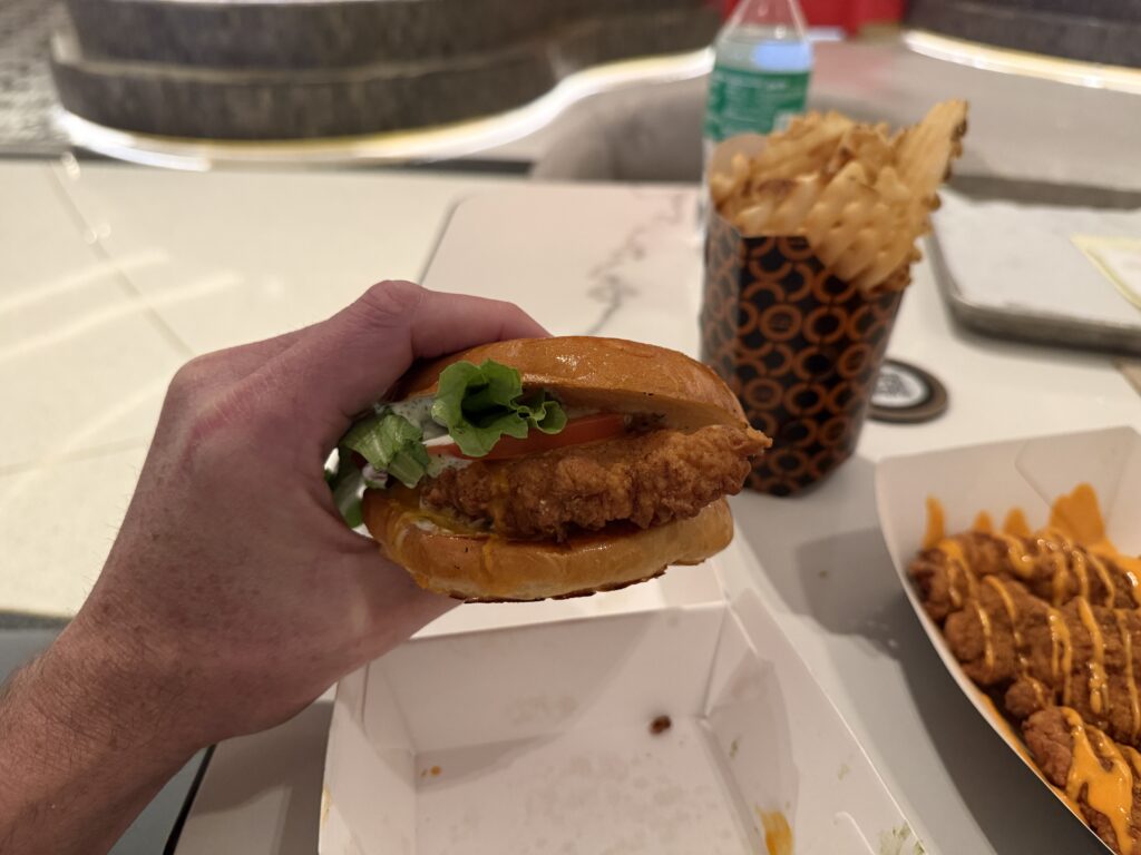 The chicken sandwich, picked up and in my hand to show the chicken, lettuce, tomato, and ranch spilling out. 