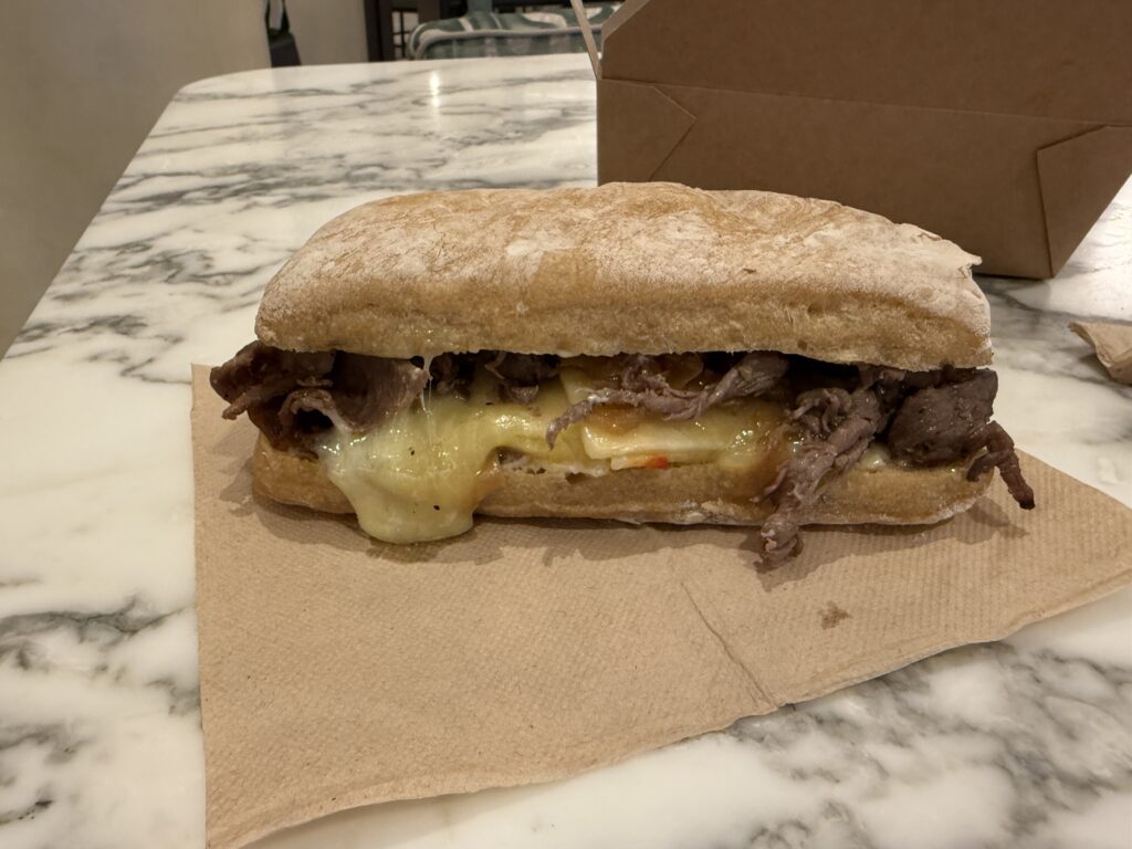 A long hoagie sandwich with melted cheese and meat spilling out of it on a table.