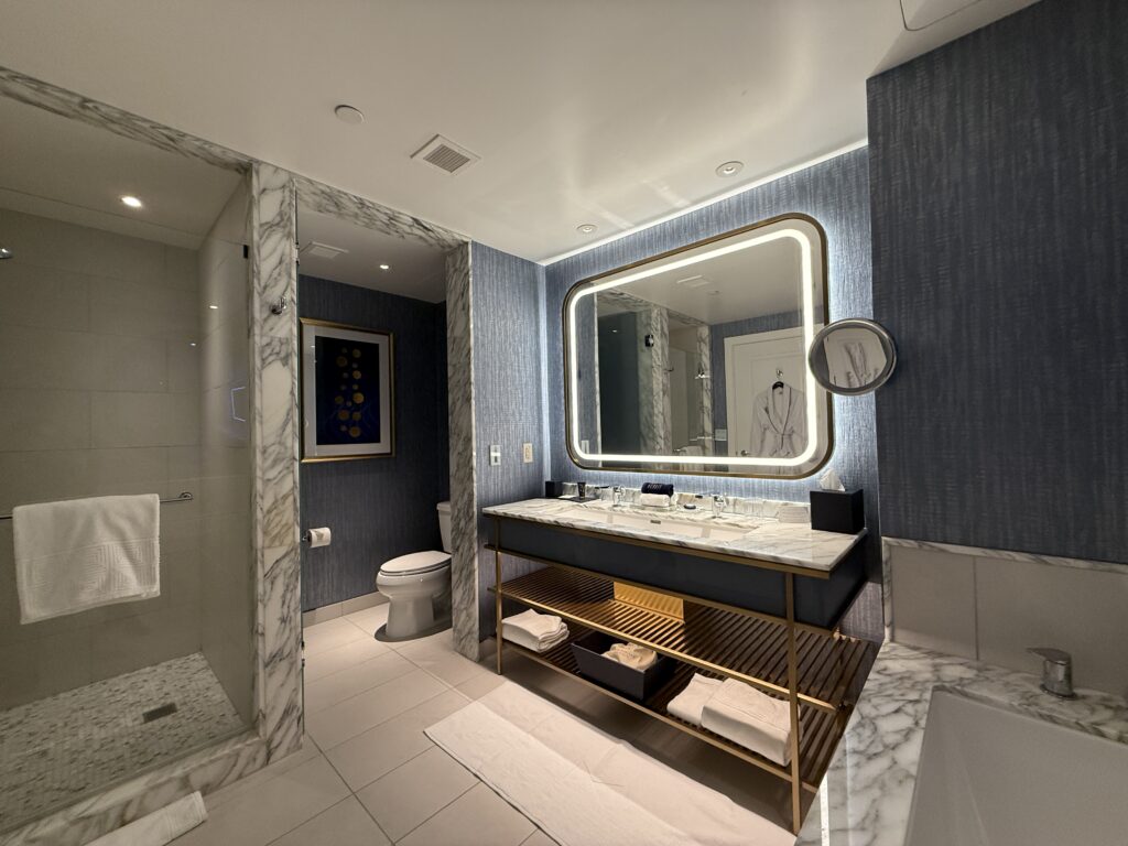 A glass shower, water closet with the toilet, and illuminated mirror above a dual faucet vanity.