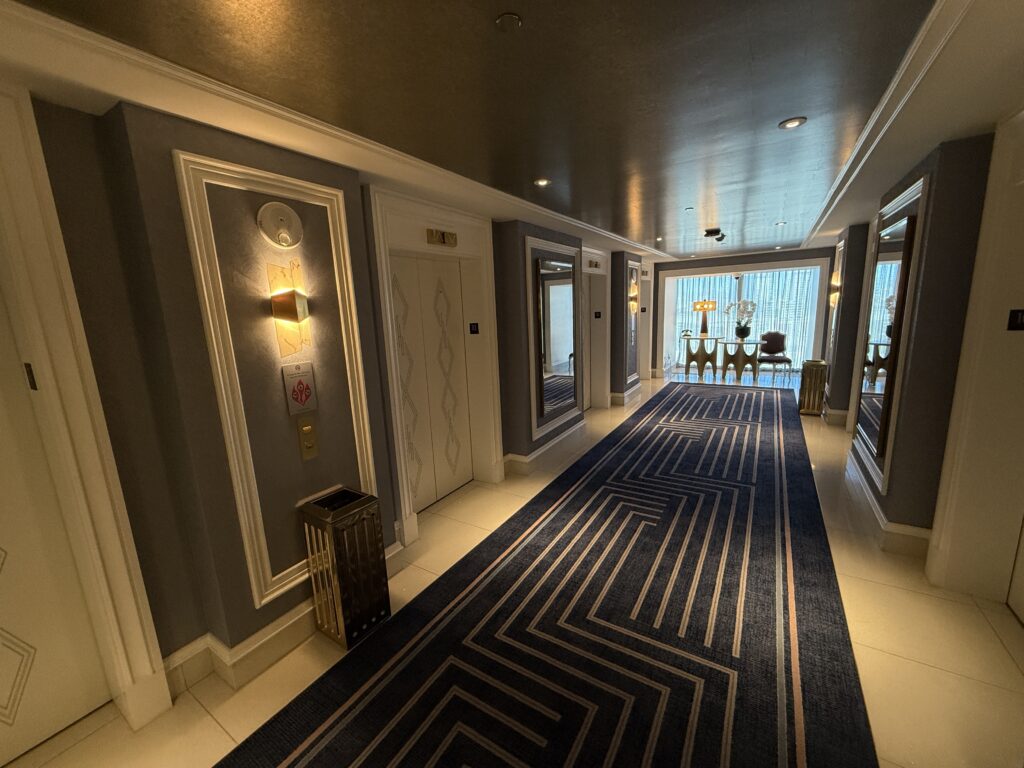 Hotel floor elevator lobby, which blue carpet, white elevator doors, and a window outside in the background. 