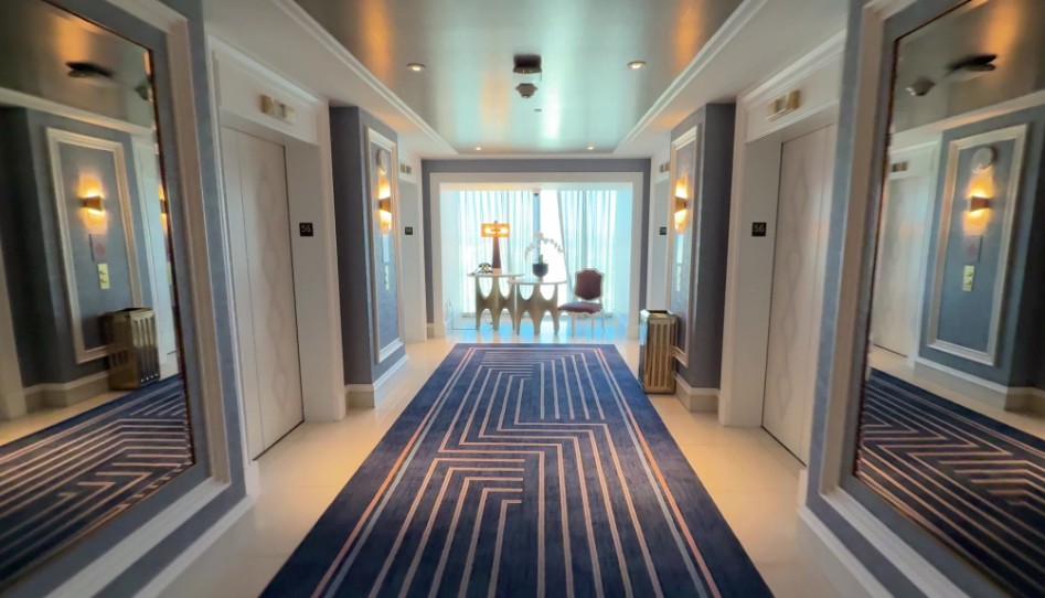 The elevator lobby on our hotel floor, with blue carpeting, gold fixtures, and a window to the outside in the background.