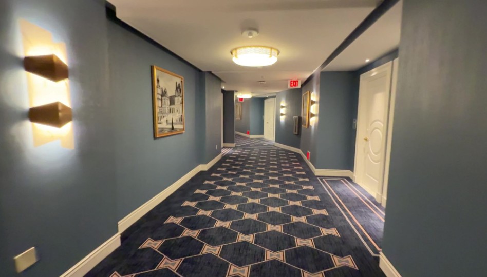 A wide hotel hallway, with bowtie carpeting and blue walls.