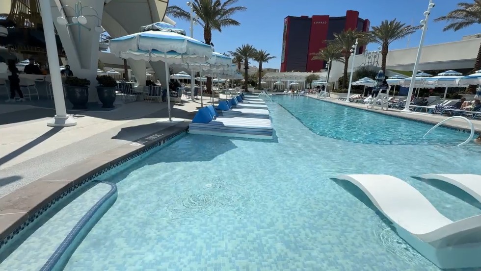 An oval shaped pool with loungers in the water, and a depeer section in the middle of the oval.