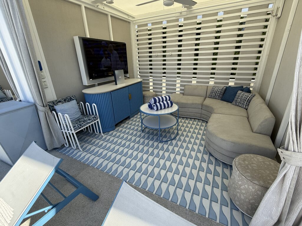 A pool cabana with seating, shade, a TV, and a fridge. 