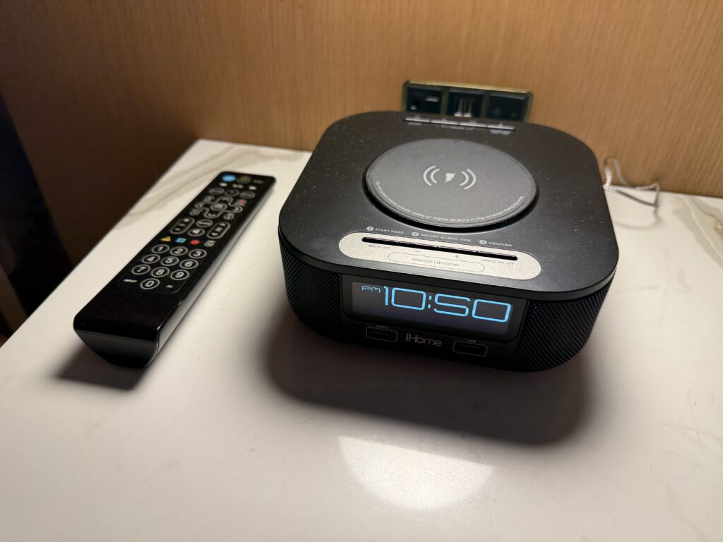 A bedside clock with a wireless charging pad atop it. 