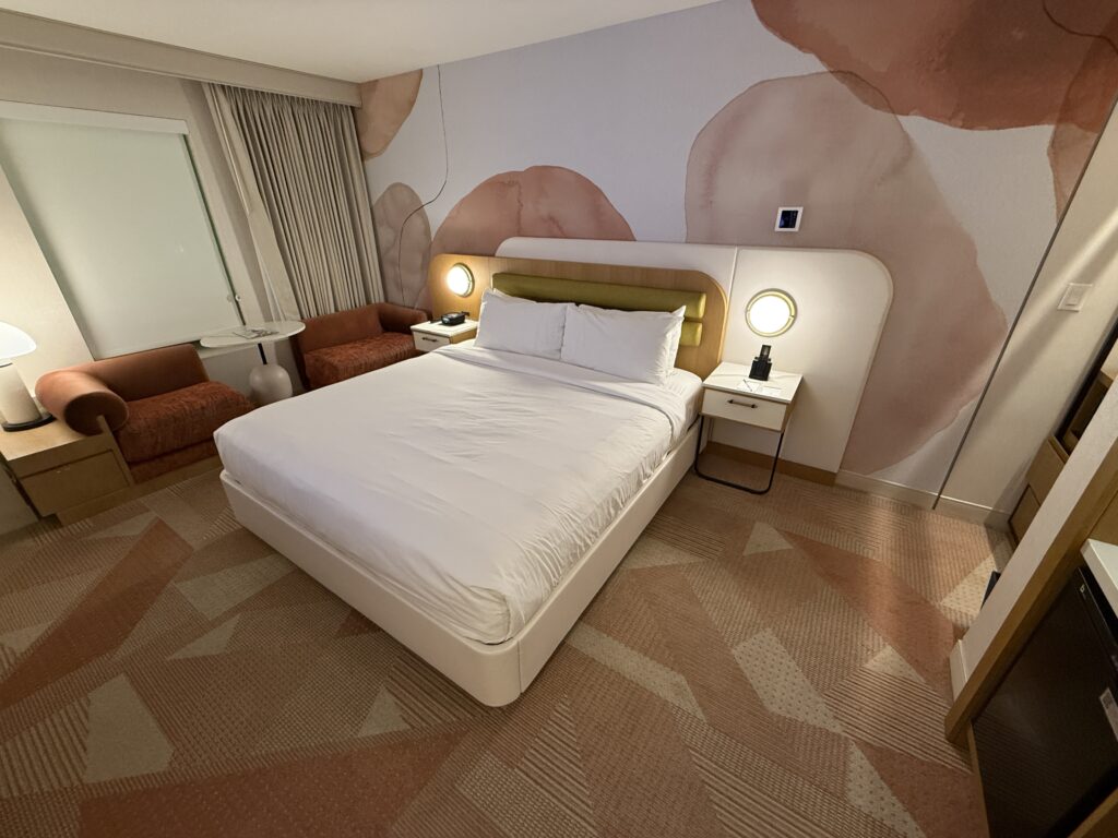 A king bed pushed up against a pink, floral themed accent wall. 