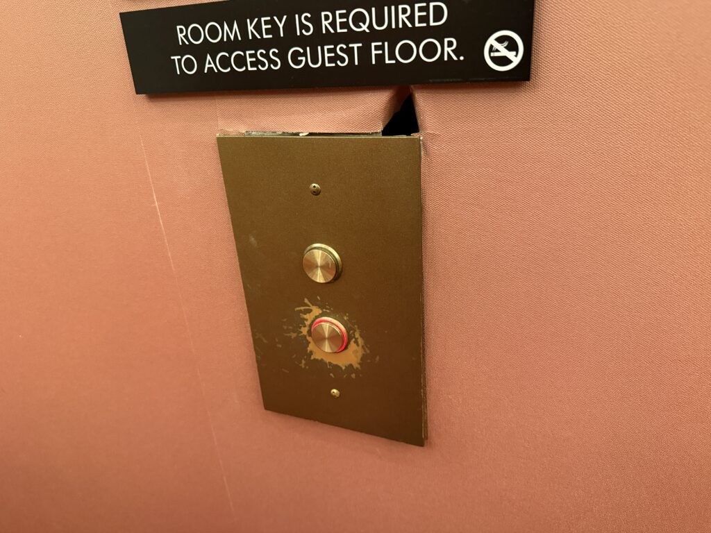 An elevator button with a hole in the wall above it. 