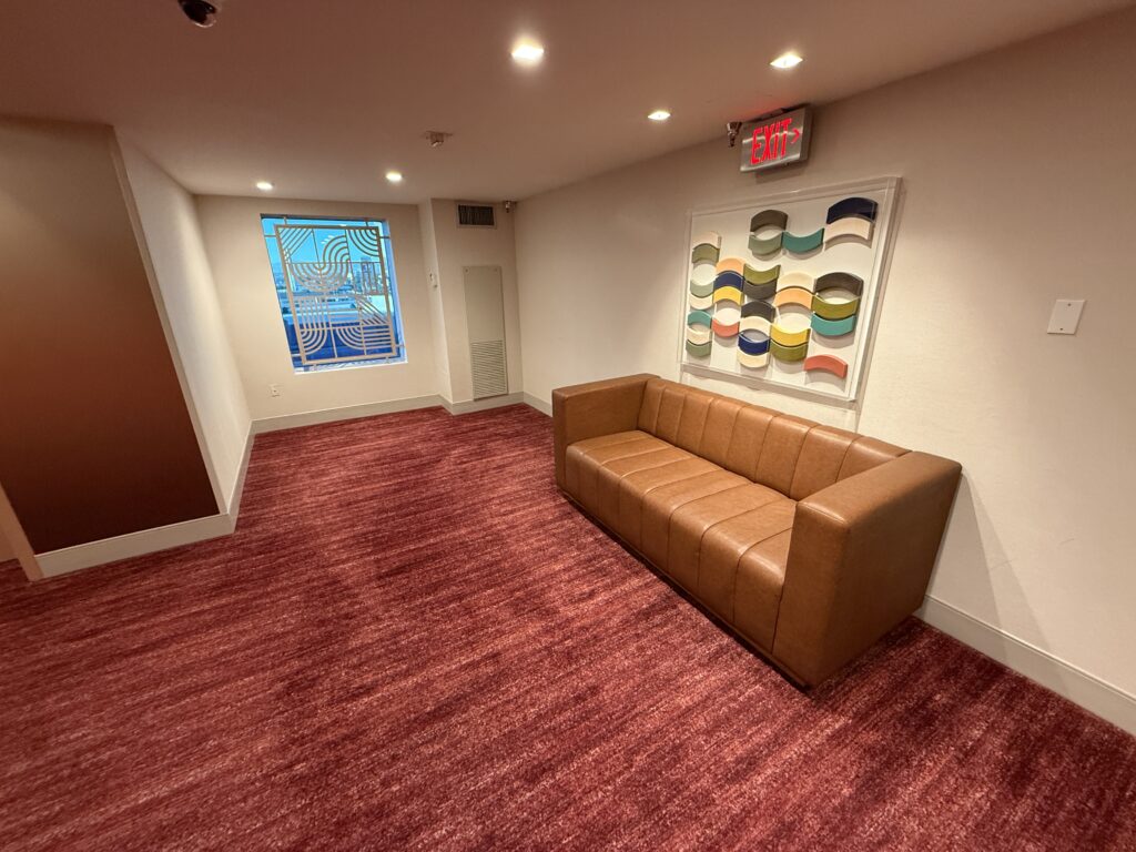 A couch in the elevator lobby with a piece of colorful art hung above it. 
