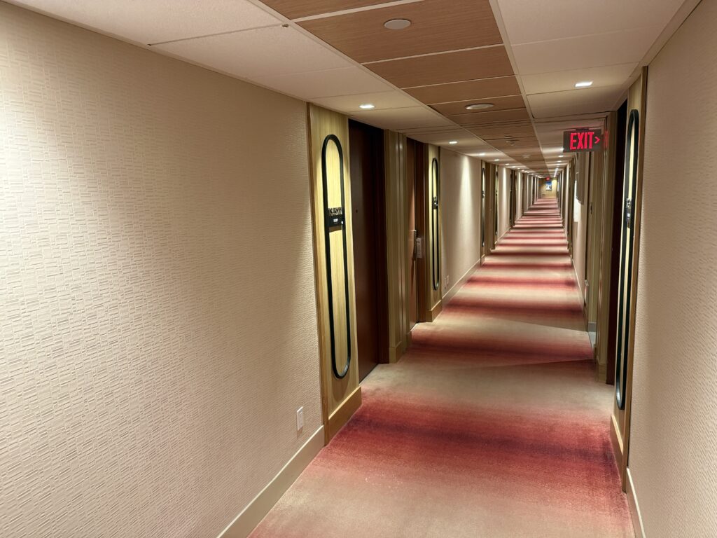 A hotel hallway, with low ceilings and pink tones. 