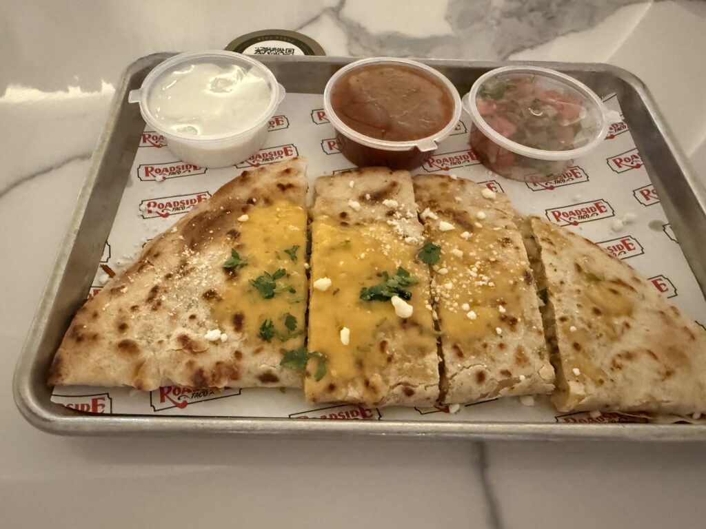 A chicken quesadilla on a tray, cut up, with 3 tubs of salsa.