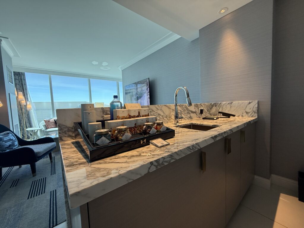 Marble countertop with a sink, and dry minibar atop it. The window to the outdoors is in the background.