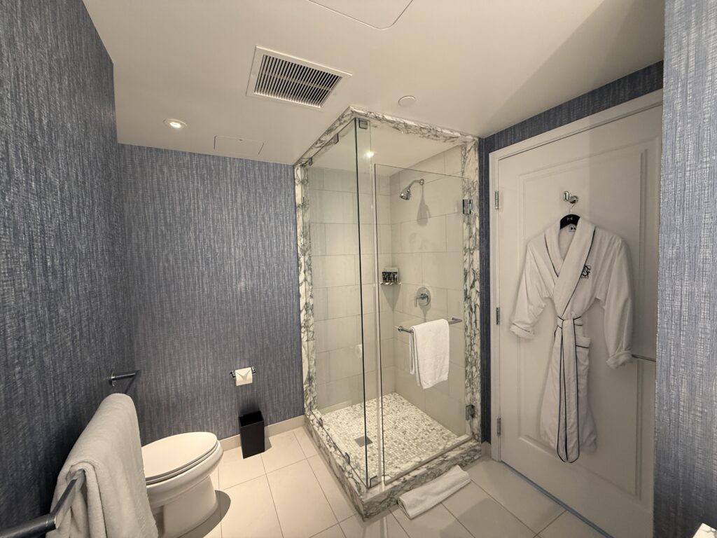 Blue textured bathroom walls with a glass corner shower and marble trim, white towels and a robe on the door