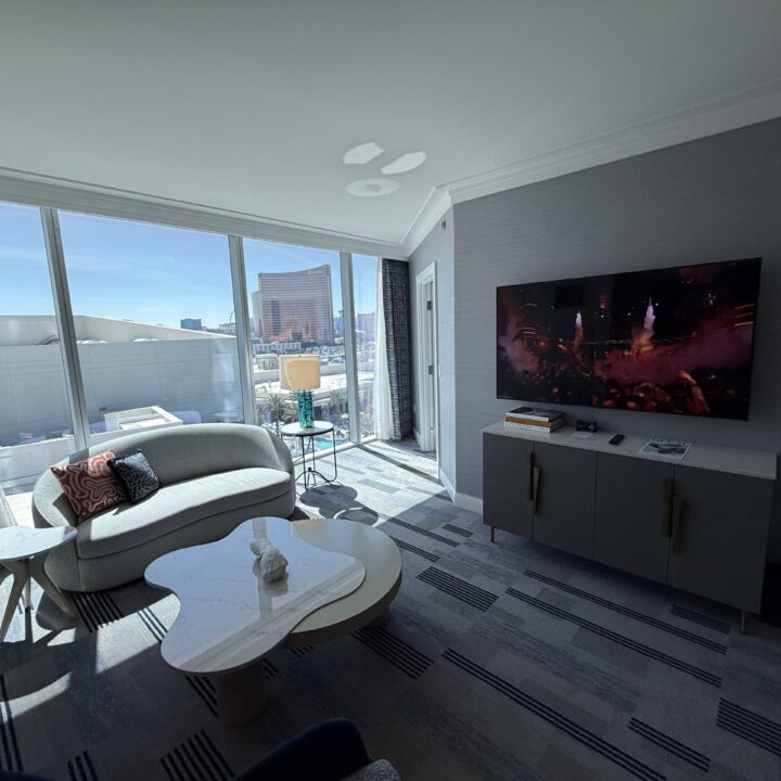 The living area, which has a small love seat, table and TV in front of floor to ceiling windows.
