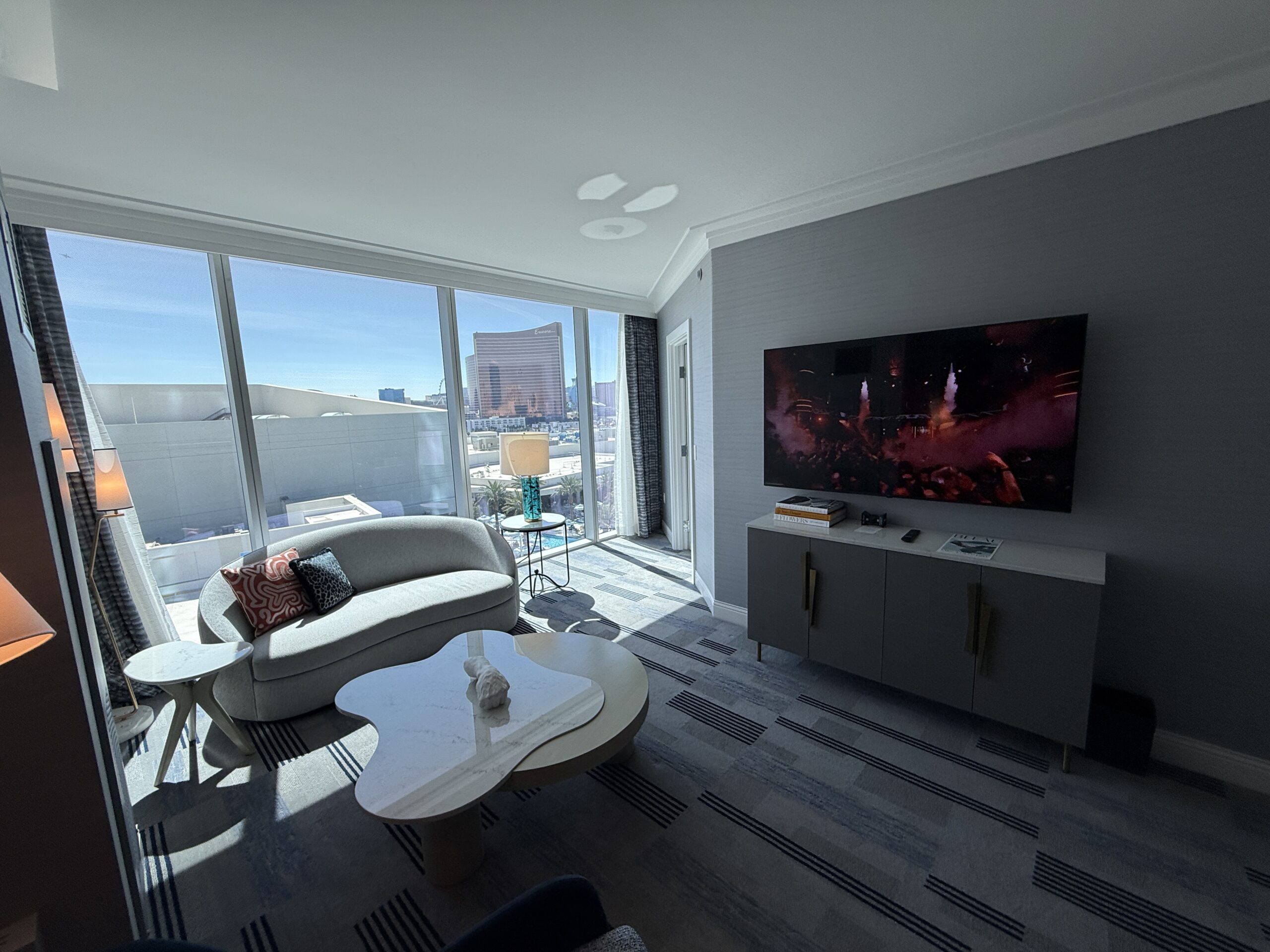 The living area, which has a small love seat, table and TV in front of floor to ceiling windows.