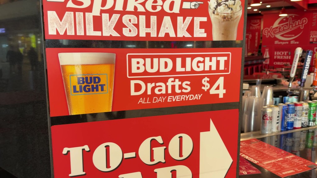 Signboard in a bar advertising Bud Light Drafts for $4 all day, with a Bud Light glass image and a large TO-GO arrow section at the bottom.
