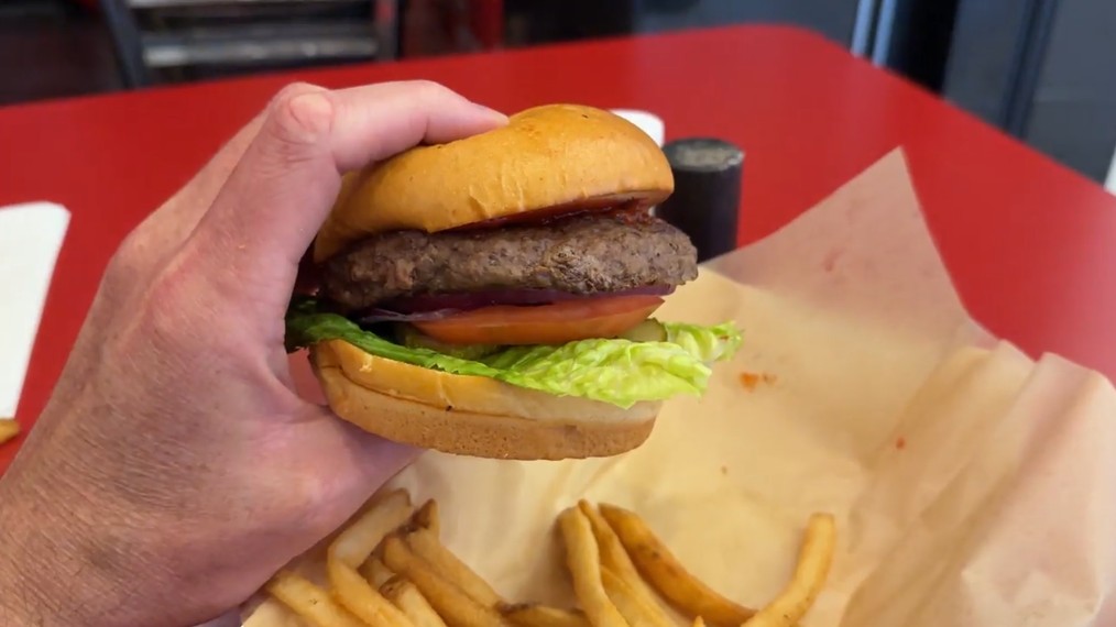 The burger, held in my large hand, stacked with veggies.