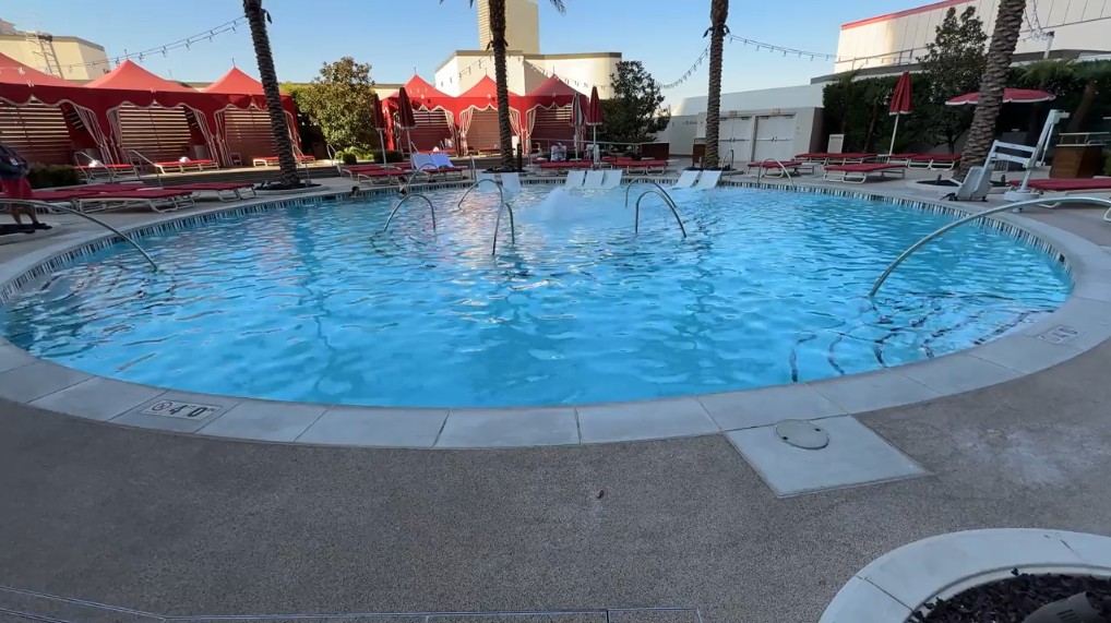 A circular pool with a fountain in the middle, surrounded by cabanas. 