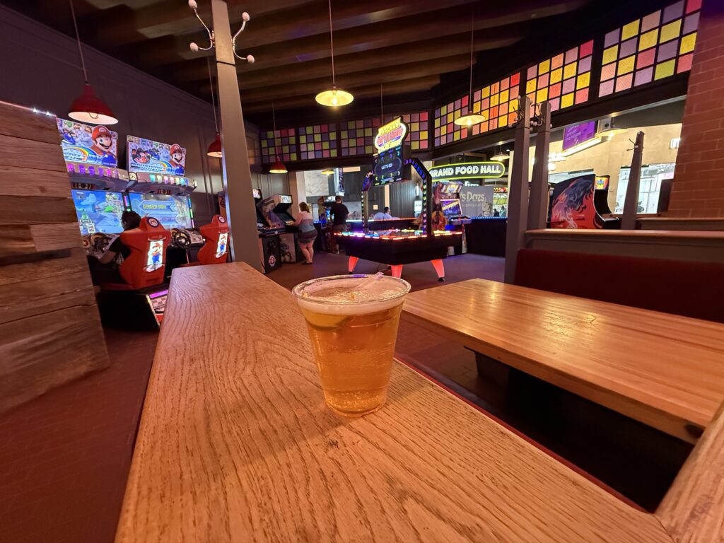 A draft beer, sitting on a ledge with arcade games in the background. 