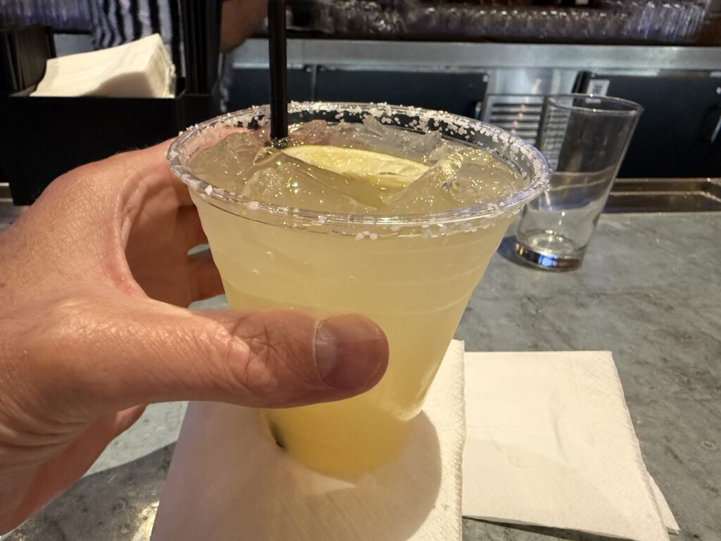 A yellow margarita in a plastic cup is in my hand. 