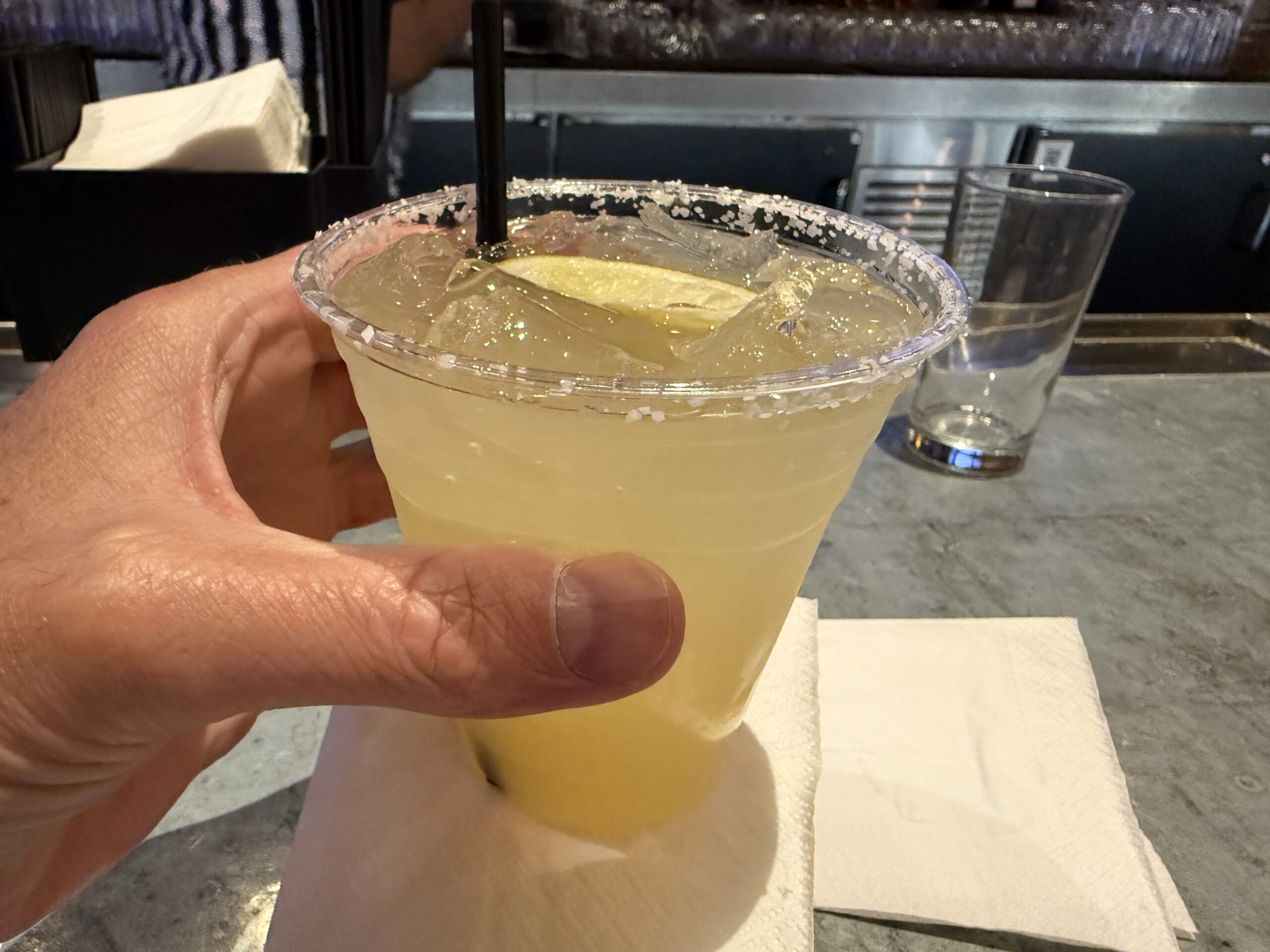A yellow margarita in a plastic cup is in my hand.