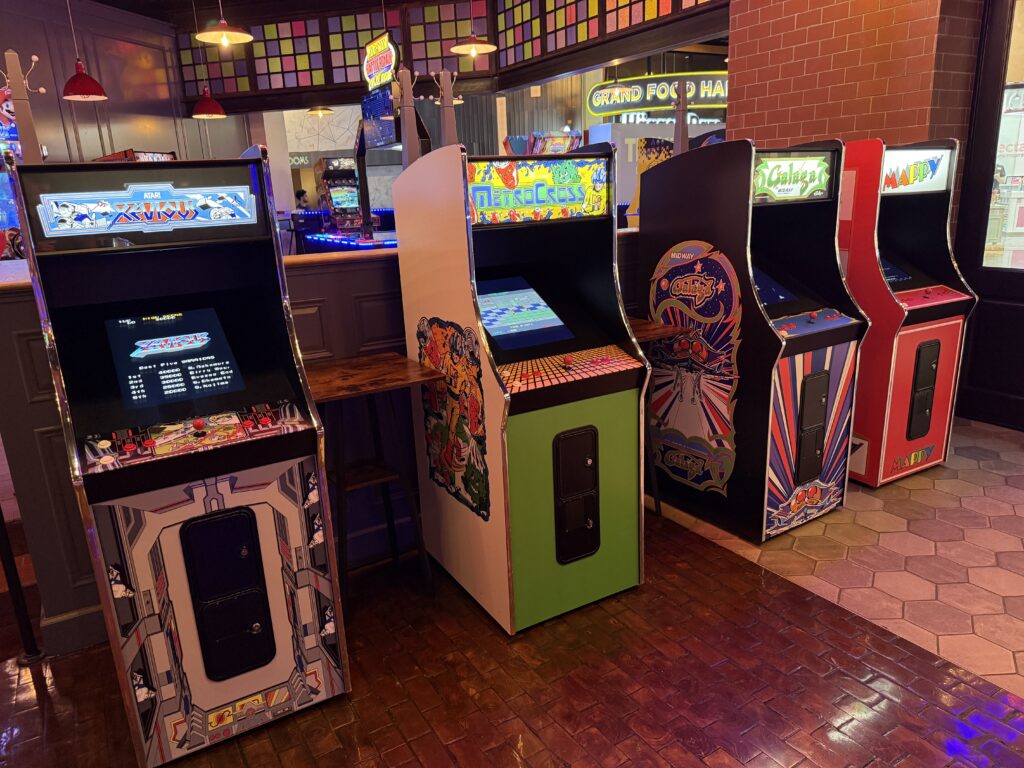 Row of vintage arcade cabinets with colorful side art in an arcade setting.