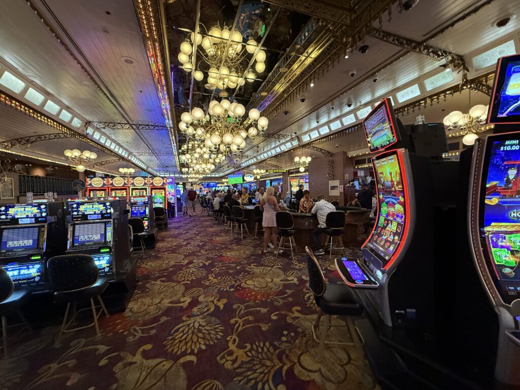 The casino floor at 4 Queens, with rows of table games and decorative chandeliers above hanging from the ceiling.