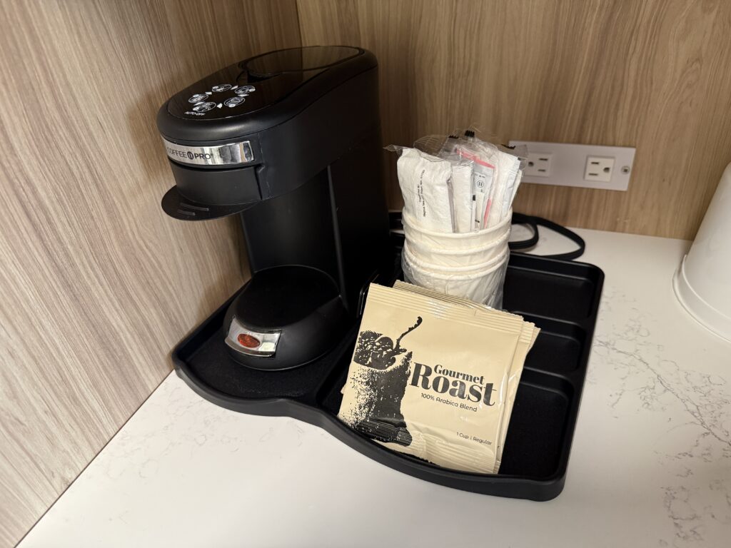 A coffee maker on a tray with several packets of free coffee.