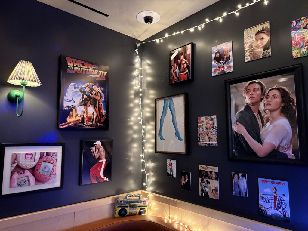 Wall decorated with framed movie posters and string lights in a cozy room. A large  poster from the movie Titanic dominates the right side by a couch.